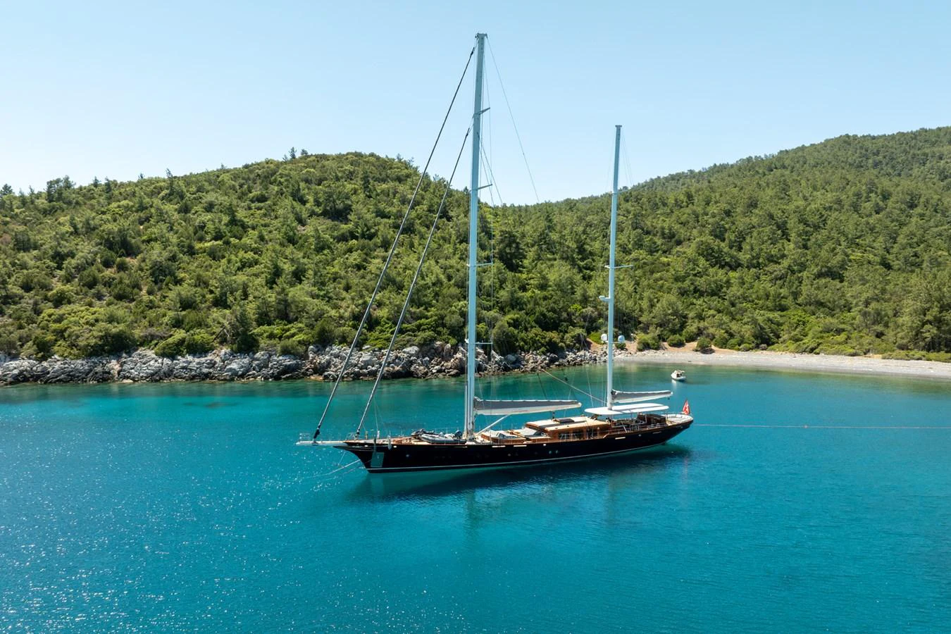 A stunning yacht is anchored in a serene bay surrounded by lush greenery and clear blue waters. aboard SALLYNA Yacht for Sale