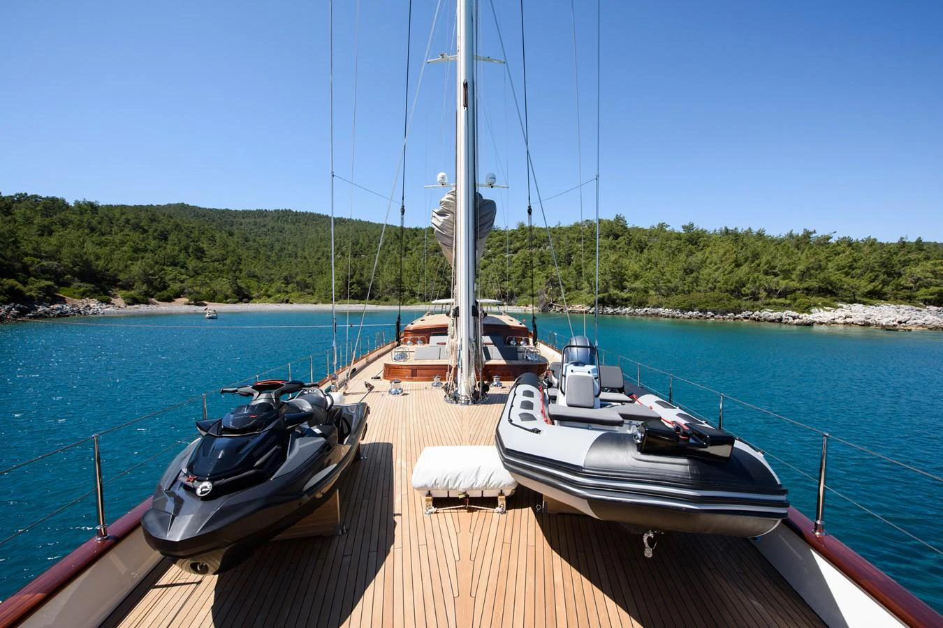 The yacht's deck features a spacious layout with jet skis and a tender, set against a serene coastal backdrop. aboard SALLYNA Yacht for Sale