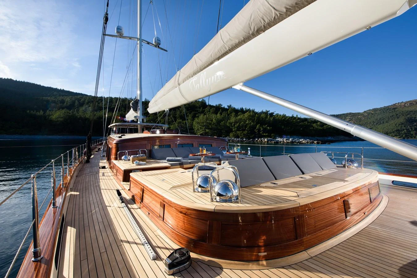 The yacht's deck features elegant wooden finishes and ample seating under clear blue skies. aboard SALLYNA Yacht for Sale