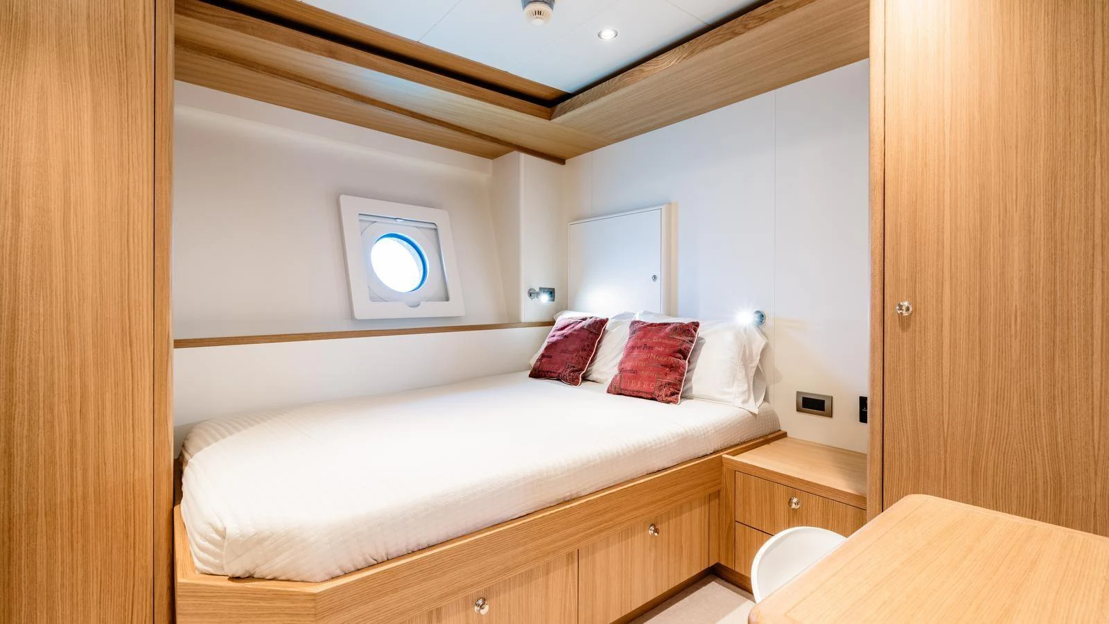 The guest stateroom features a cozy bed with elegant wooden finishes and a porthole for natural light. aboard MIDNIGHT SAGA Yacht for Sale