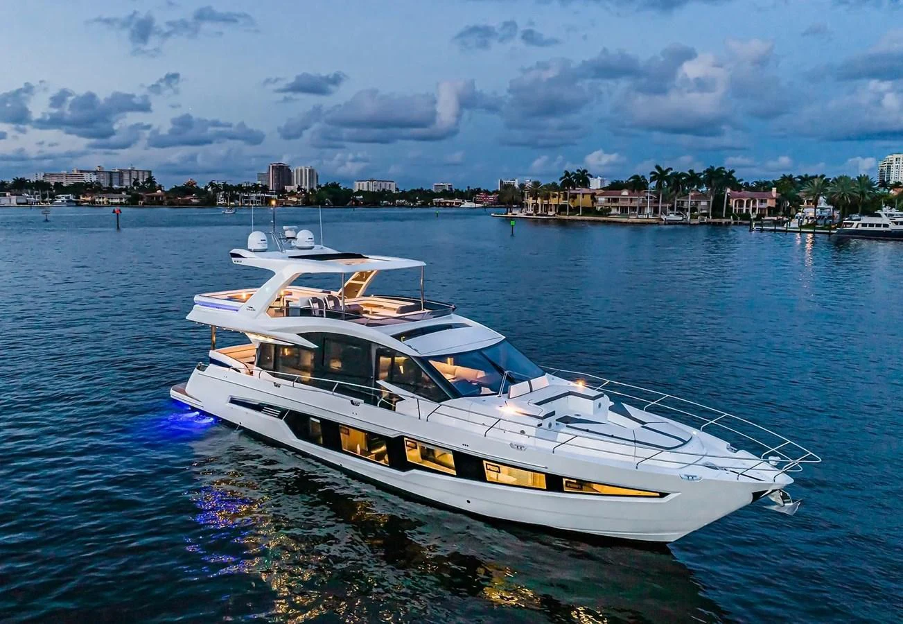 A sleek and modern yacht cruises gracefully on calm waters at dusk, illuminated by soft ambient lighting. aboard VIRTUS Yacht for Sale