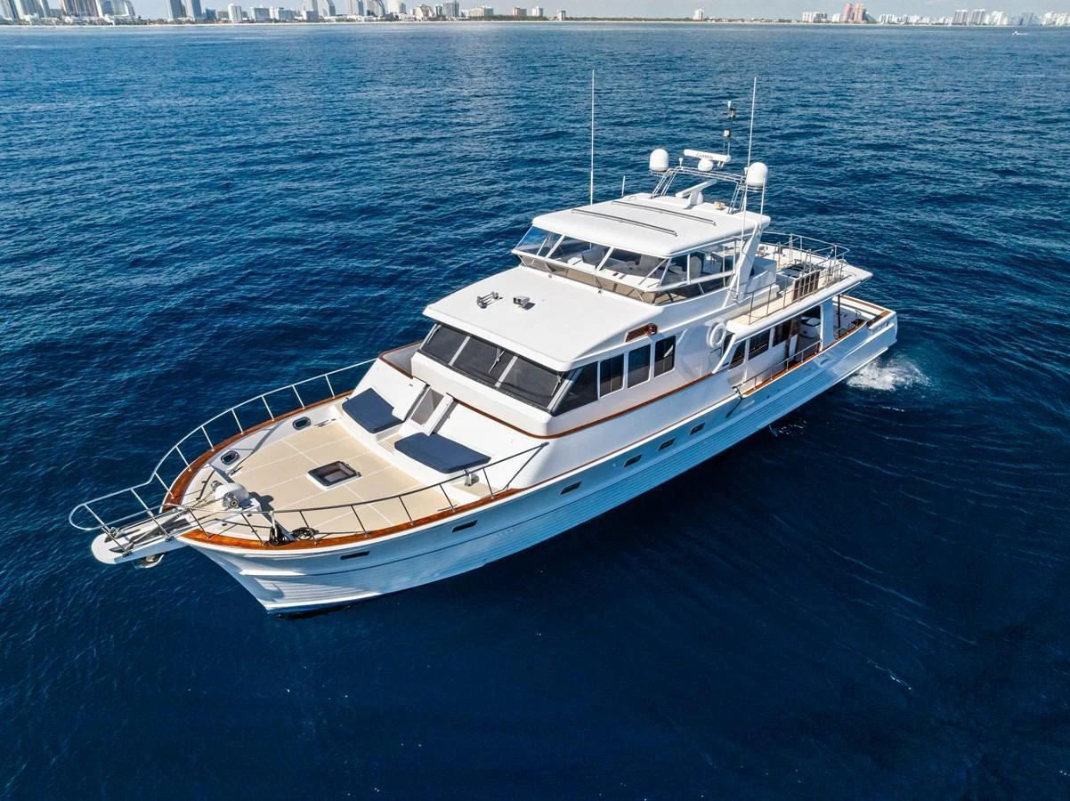 A luxurious yacht cruises through the deep blue waters with a cityscape in the background. aboard EL LEGADO Yacht for Sale