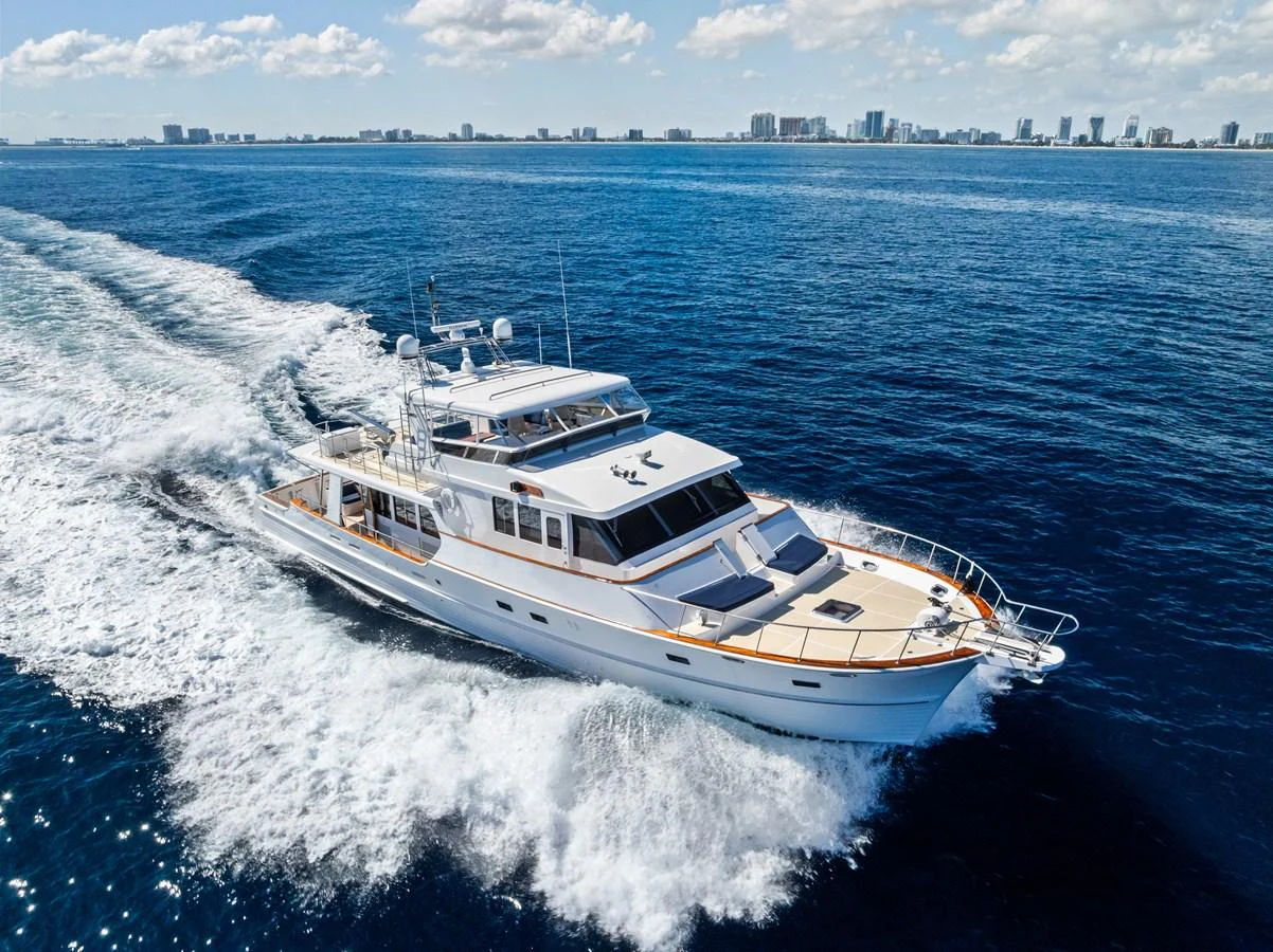 A sleek yacht cruises through the open water with a city skyline in the background. aboard EL LEGADO Yacht for Sale