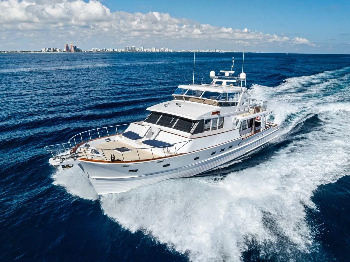 A luxurious yacht cruises through the open sea with a cityscape in the background. aboard EL LEGADO Yacht for Sale