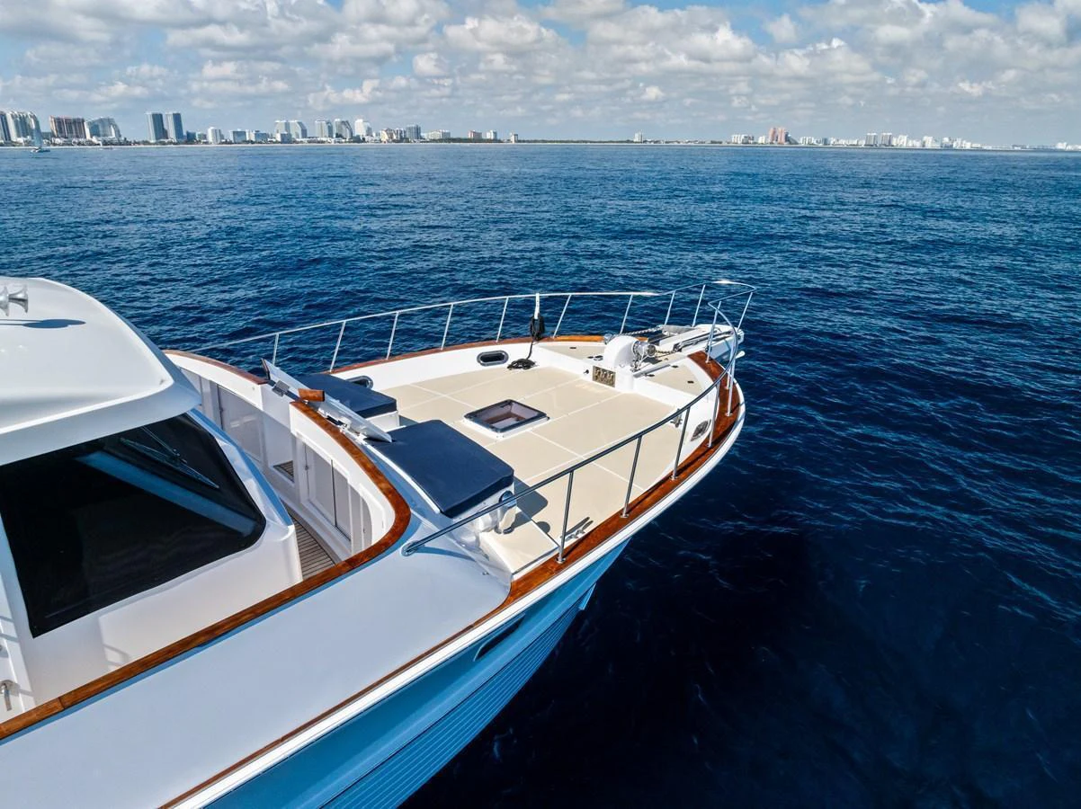A sleek yacht cruises through deep blue waters with a cityscape in the background. aboard EL LEGADO Yacht for Sale