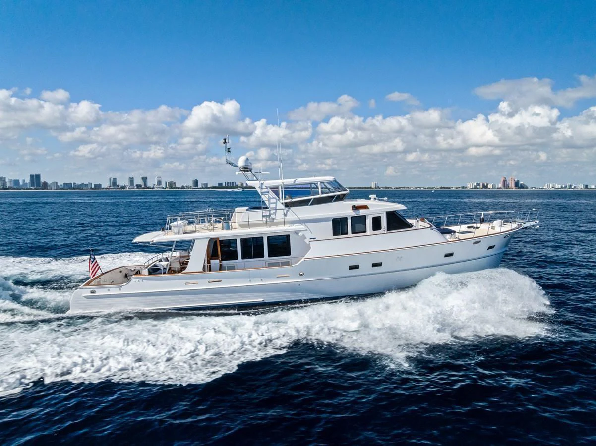 A luxurious yacht cruises through the open water with a city skyline in the background. aboard EL LEGADO Yacht for Sale
