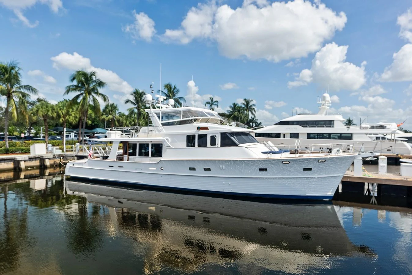 A classic yacht is docked in a serene marina under a bright blue sky with fluffy clouds. aboard EL LEGADO Yacht for Sale