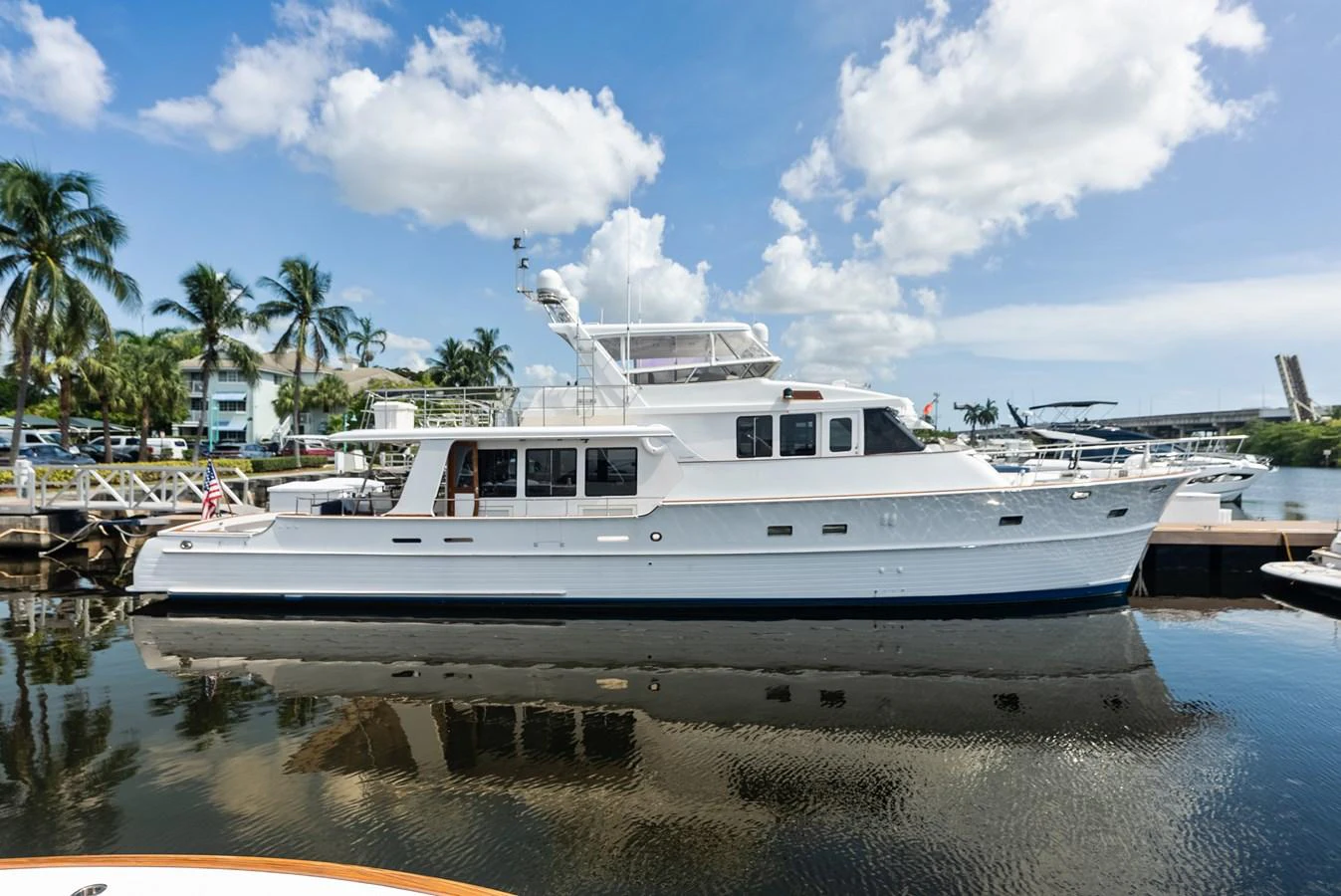 A classic yacht is docked at a marina under a bright blue sky with scattered clouds. aboard EL LEGADO Yacht for Sale