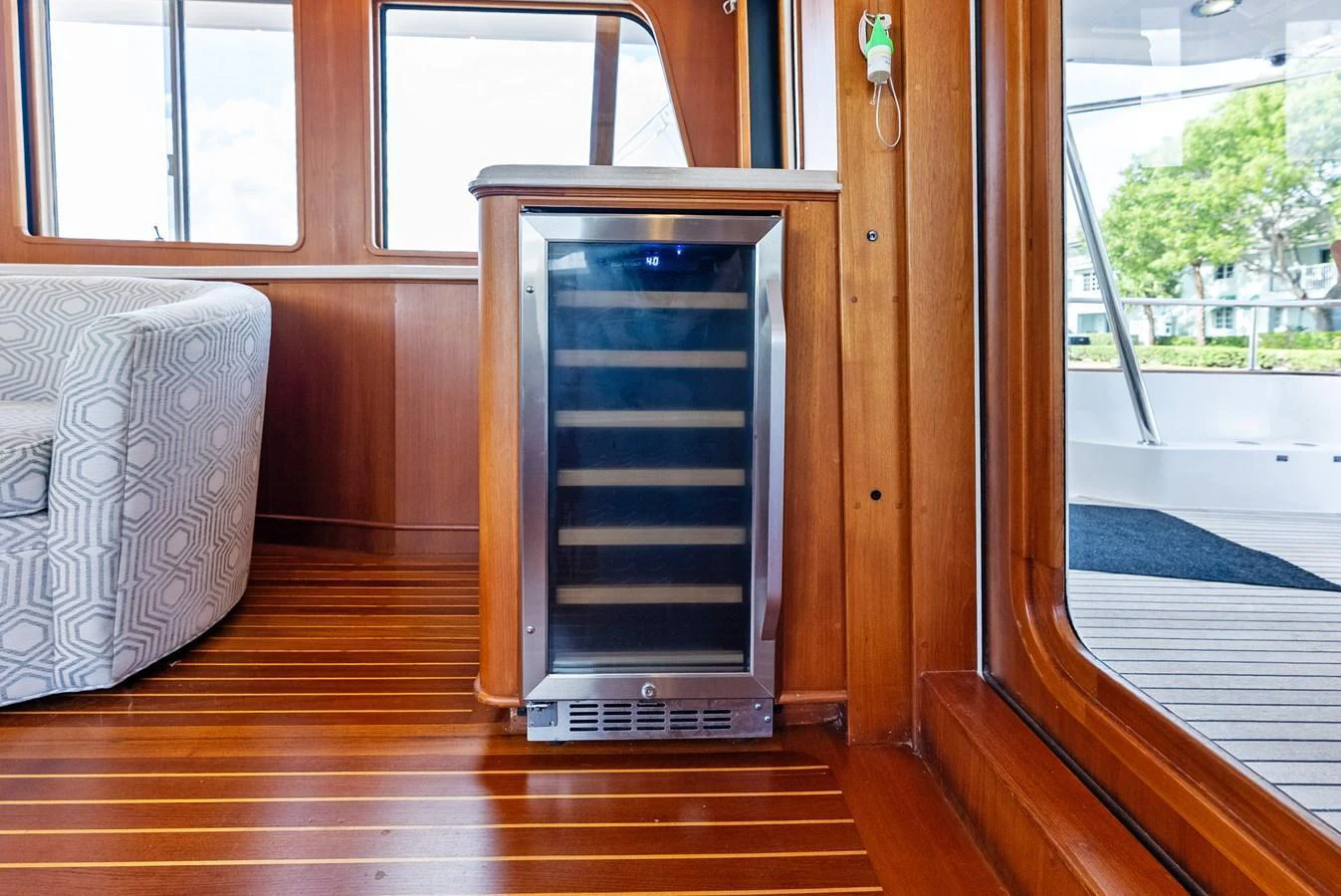 The image showcases a stylish interior with a wine cooler and wooden flooring, leading to an exterior deck area. aboard EL LEGADO Yacht for Sale