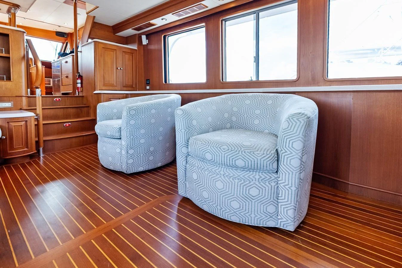 The yacht's interior features a cozy seating area with two patterned armchairs and wooden flooring. aboard EL LEGADO Yacht for Sale