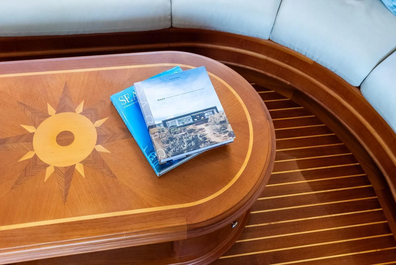 A beautifully crafted wooden table with nautical-themed inlay, accompanied by magazines, sits in a cozy seating area. aboard EL LEGADO Yacht for Sale