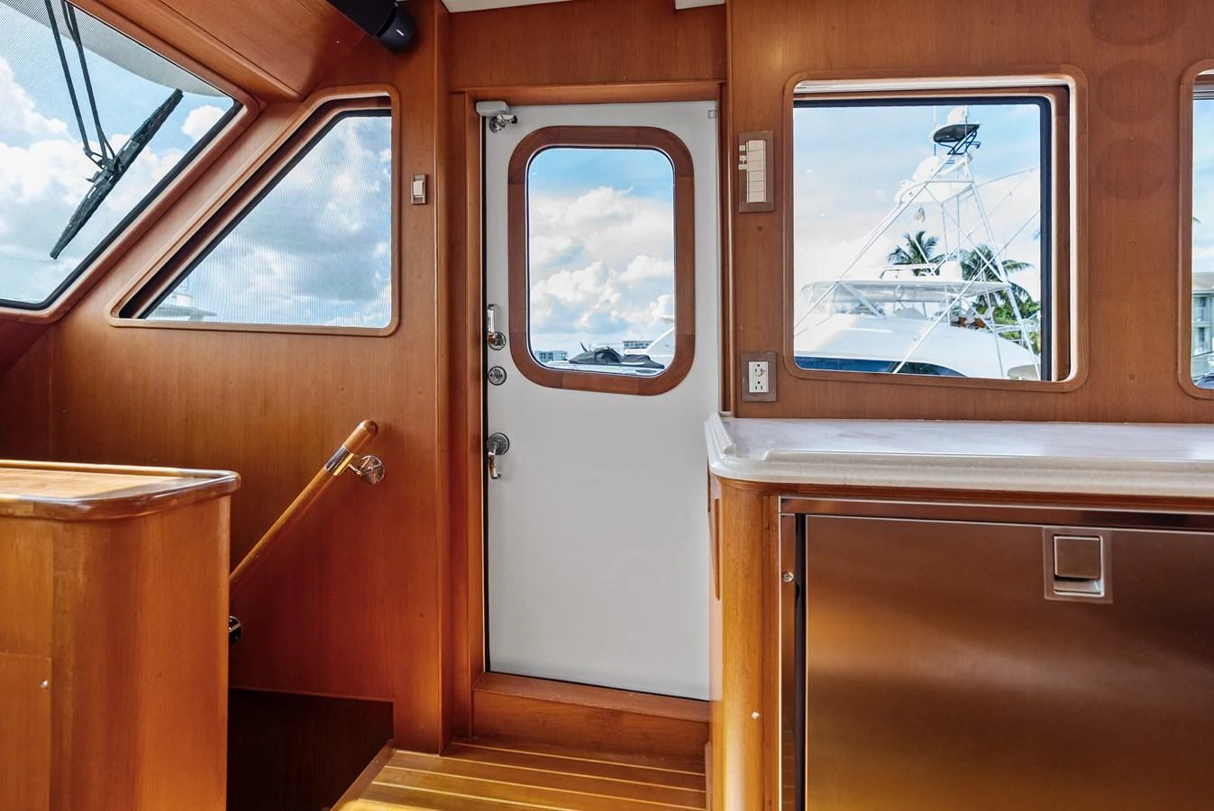 The interior features a wooden staircase and a door leading to the exterior, with a view of another yacht through the window. aboard EL LEGADO Yacht for Sale