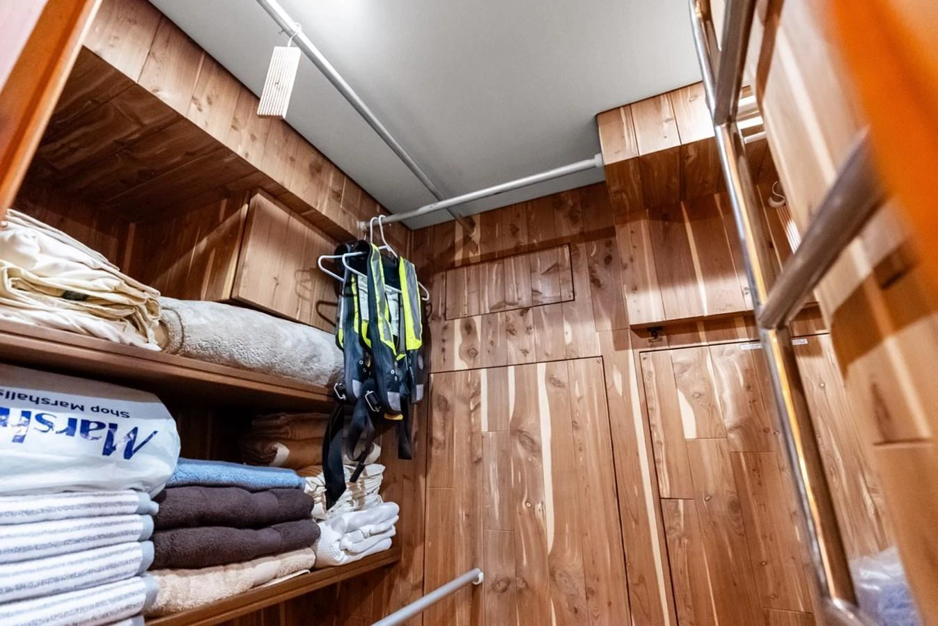 A well-organized storage area with wooden paneling and neatly arranged linens and life jackets. aboard EL LEGADO Yacht for Sale