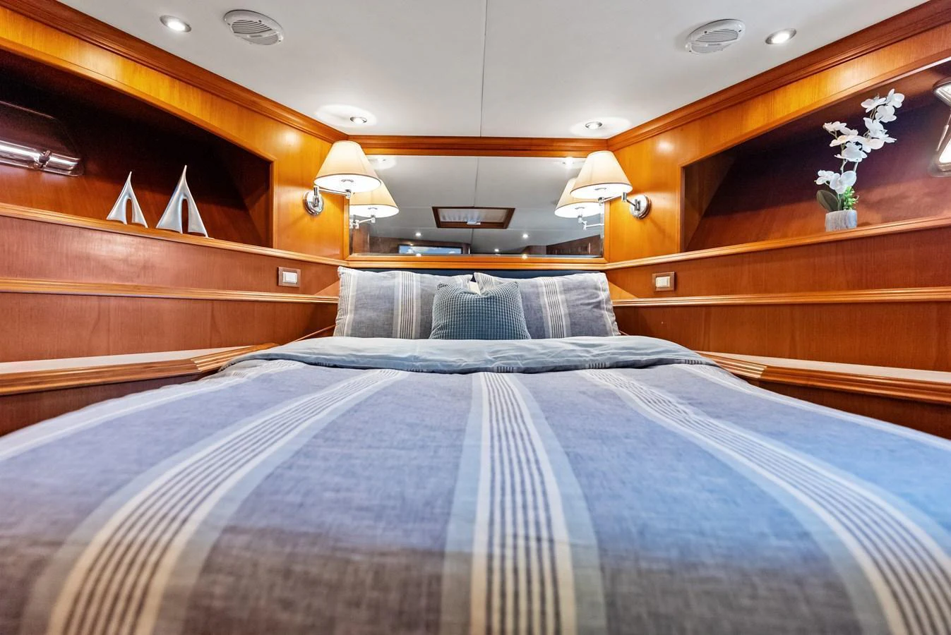 A cozy stateroom featuring a comfortable bed with striped bedding and warm wood accents. aboard EL LEGADO Yacht for Sale