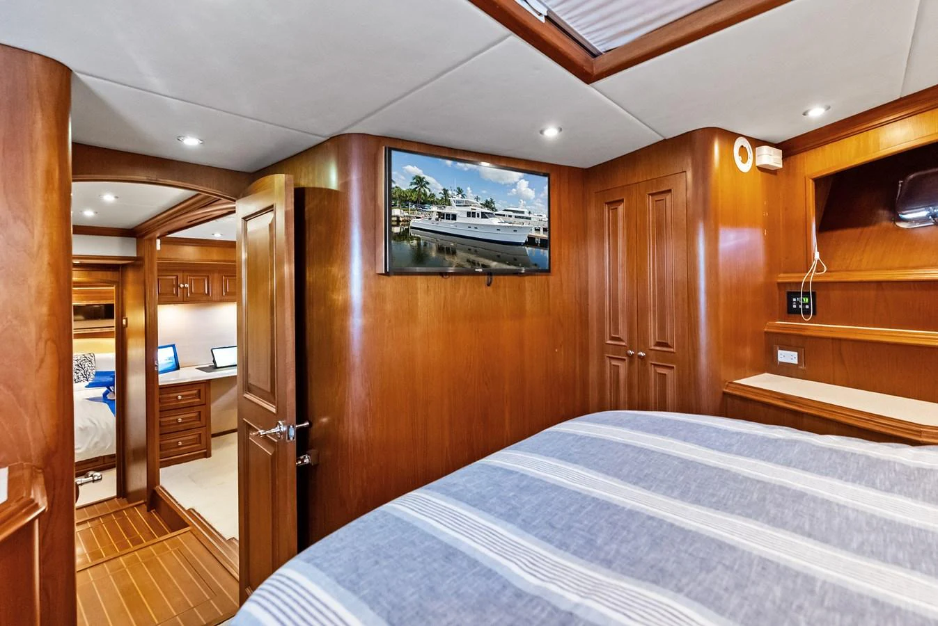 The stateroom features warm wood paneling, a comfortable bed, and modern amenities including a flat-screen TV. aboard EL LEGADO Yacht for Sale