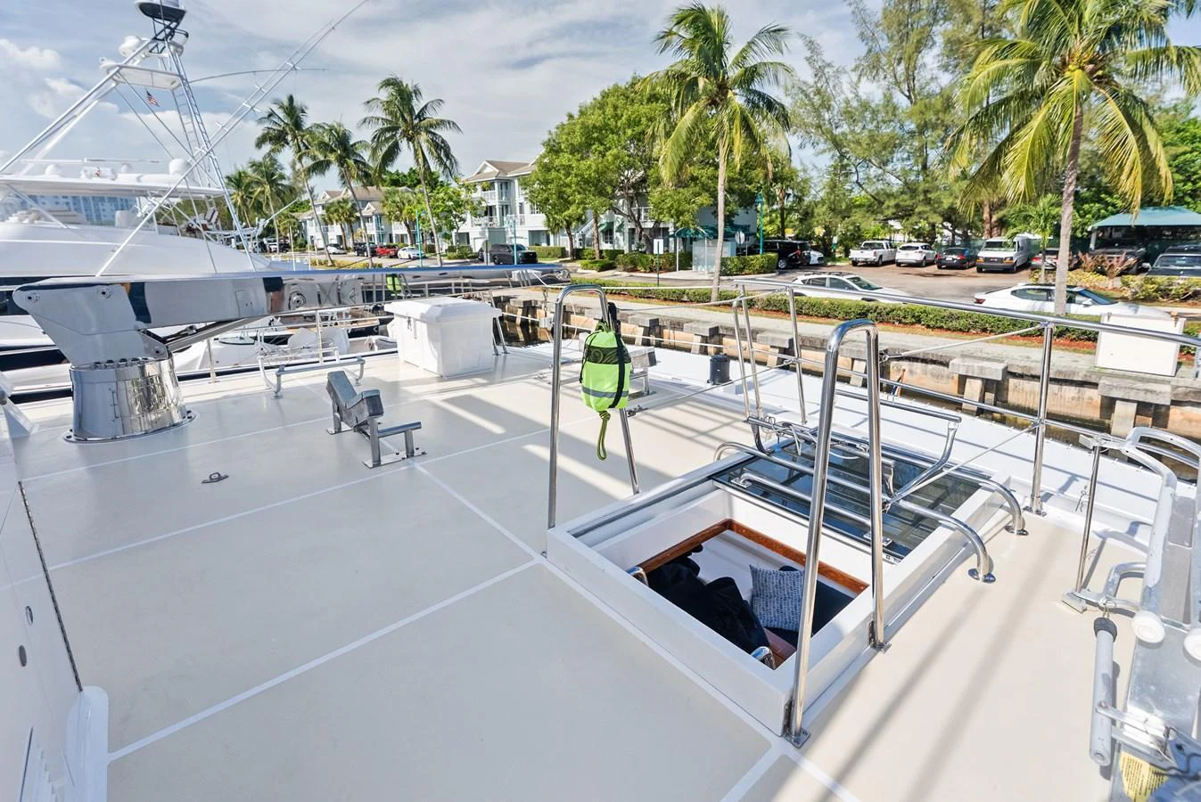 The yacht's spacious deck offers ample room for relaxation and activities, set against a backdrop of a marina and palm trees. aboard EL LEGADO Yacht for Sale