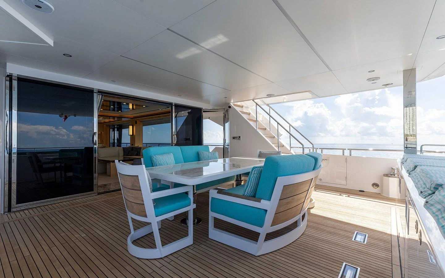 The aft deck features a stylish dining area with turquoise cushioned chairs and a sleek table, perfect for alfresco meals. aboard WADDLE WE DO Yacht for Sale
