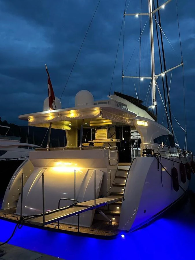 The yacht's aft deck is beautifully illuminated with blue underwater lights, creating a striking ambiance against the evening sky. aboard 23 M MOTORSAILOR Yacht for Sale