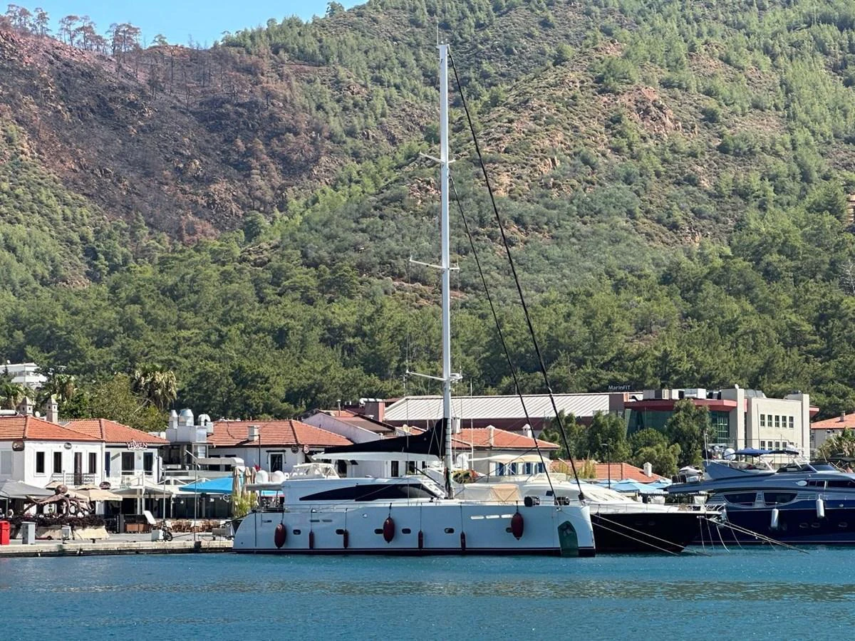 A sleek yacht is anchored in a serene marina with lush hills in the background. aboard 23 M MOTORSAILOR Yacht for Sale
