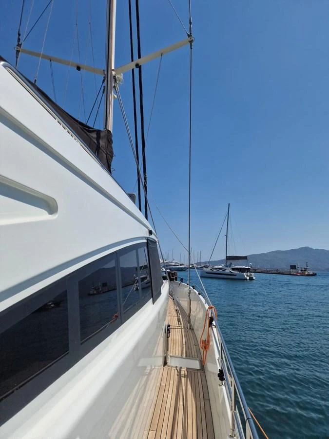 The yacht's side deck offers a sleek view of the vessel against a serene marina backdrop. aboard 23 M MOTORSAILOR Yacht for Sale