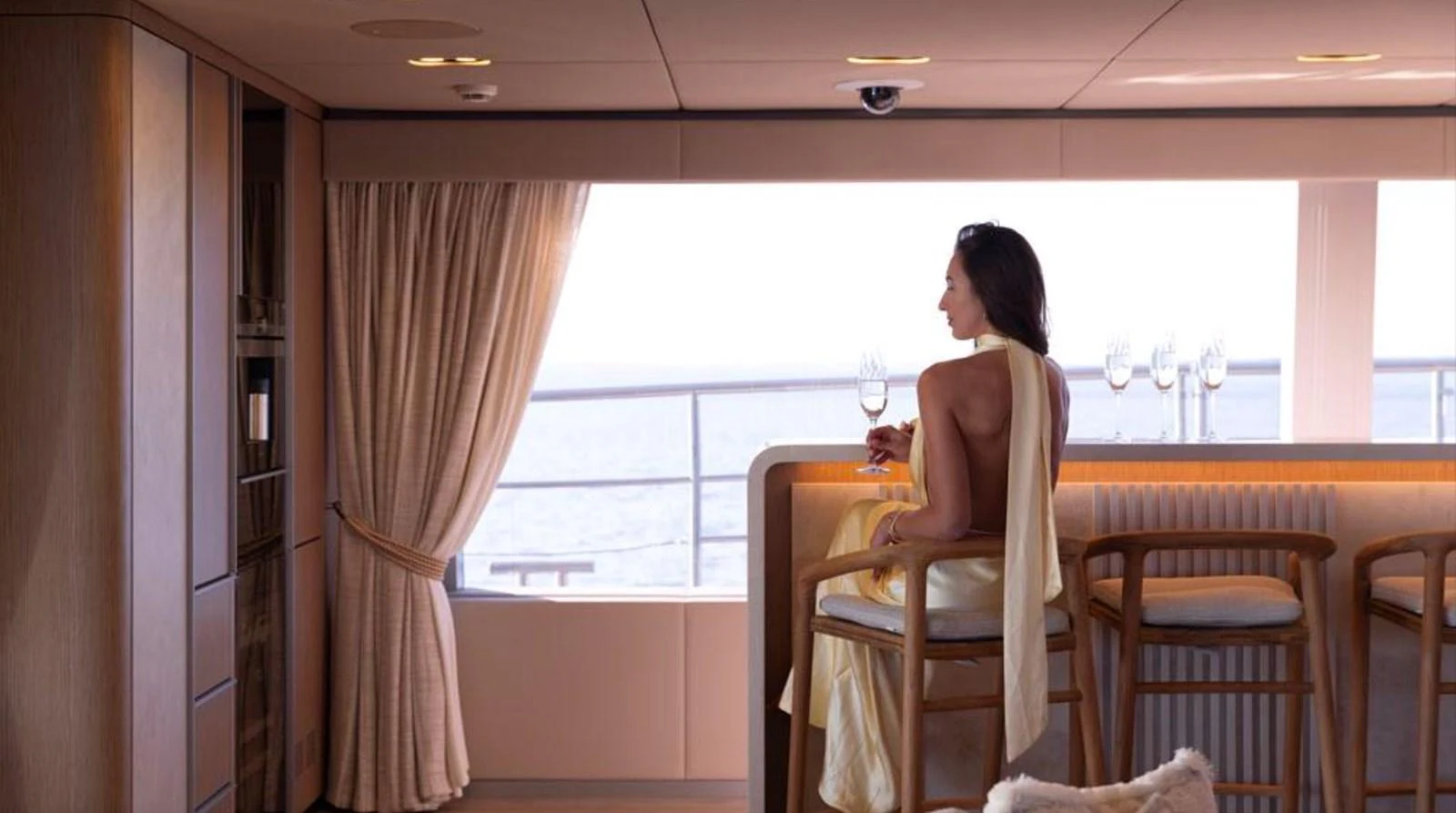 A serene interior space with a woman enjoying a drink by the window, offering a glimpse of the sea outside. aboard TWILIGHT Yacht for Sale