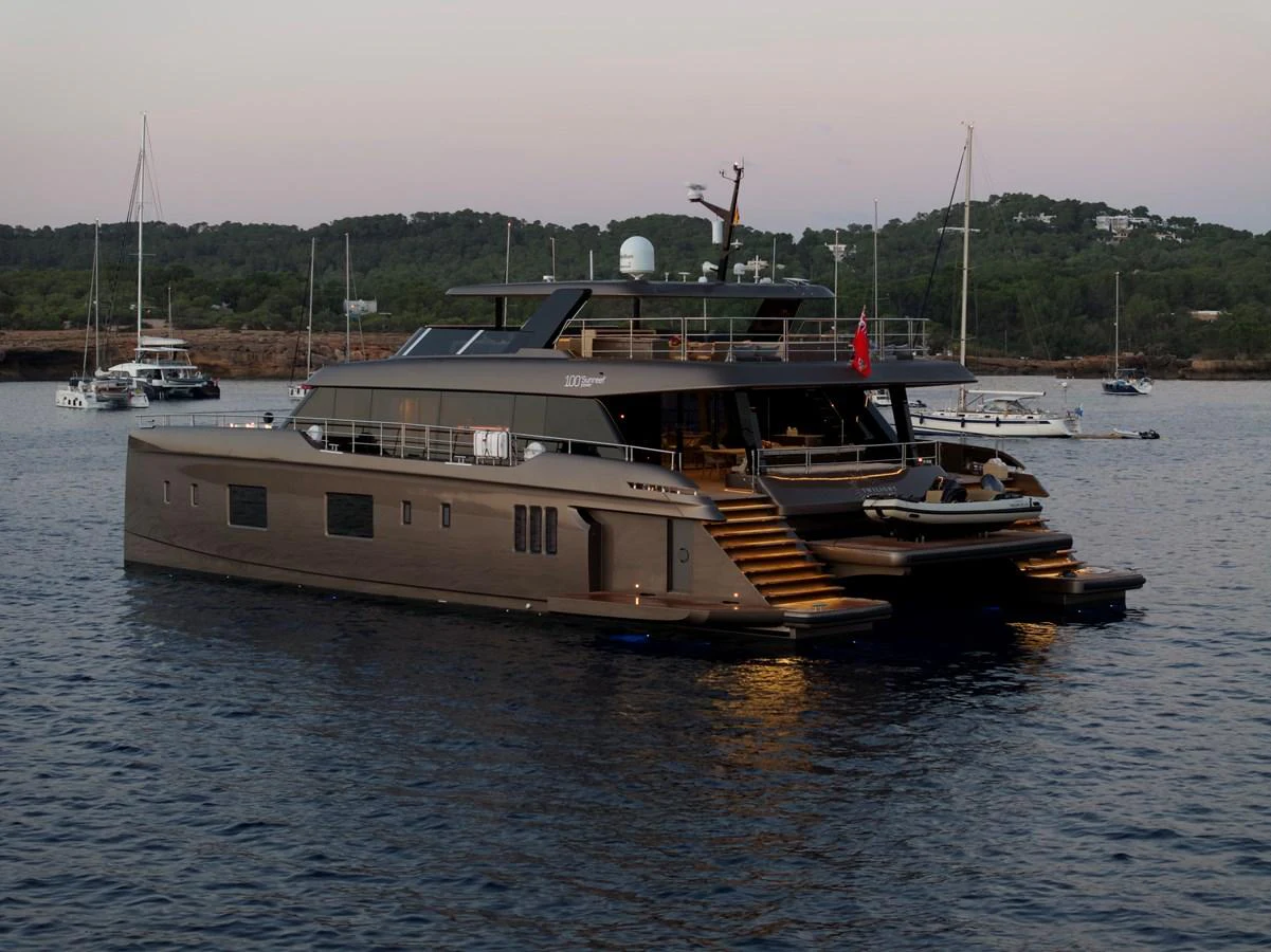 A sleek and modern yacht is anchored in a serene bay, showcasing its elegant design and spacious aft deck. aboard TWILIGHT Yacht for Sale