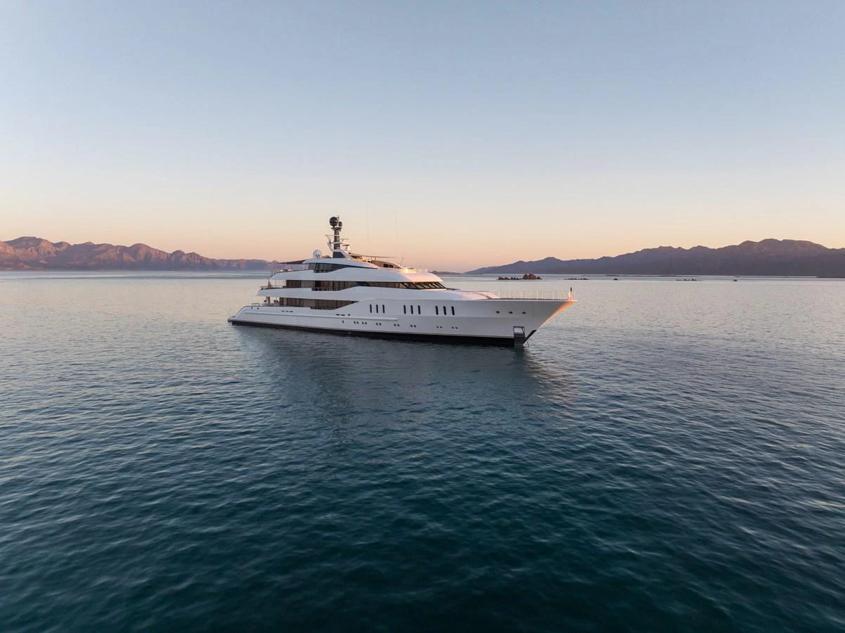 A sleek and luxurious yacht glides gracefully on calm waters against a serene mountain backdrop. aboard HAMPSHIRE Yacht for Sale