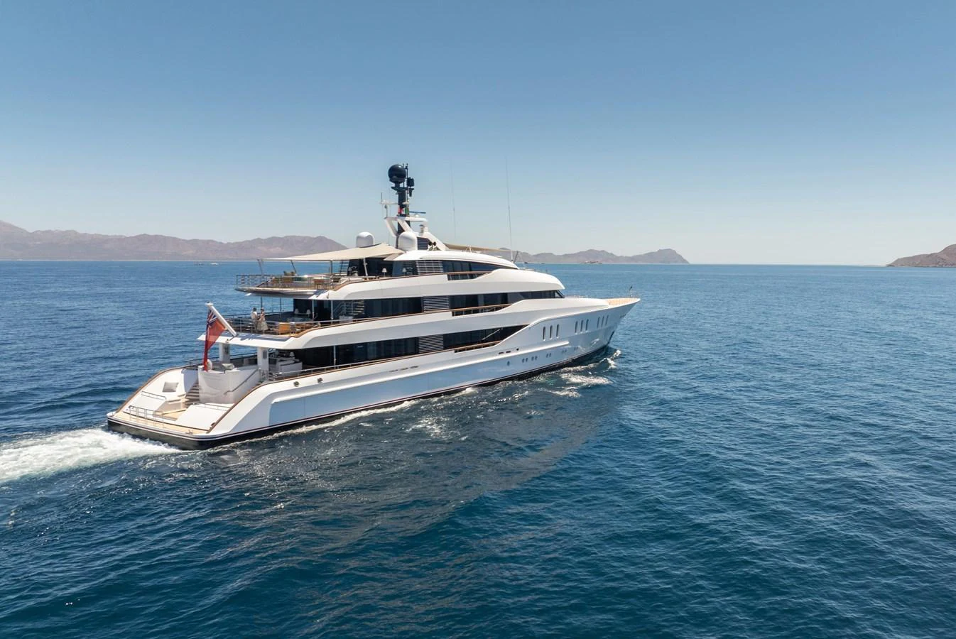 A sleek and modern yacht cruising through clear blue waters with a stunning backdrop of distant mountains. aboard HAMPSHIRE Yacht for Sale