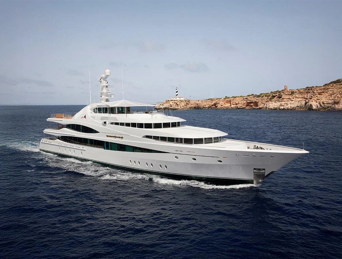 A sleek and modern yacht cruises through calm waters near a rocky coastline. aboard LADY CHRISTINE Yacht for Sale