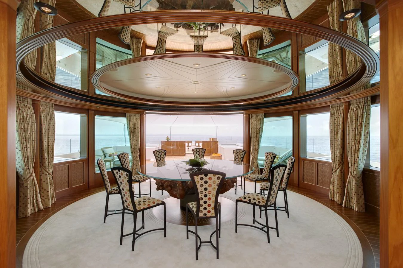 The elegant dining area features a round table surrounded by stylish chairs, with panoramic windows offering stunning sea views. aboard LADY CHRISTINE Yacht for Sale