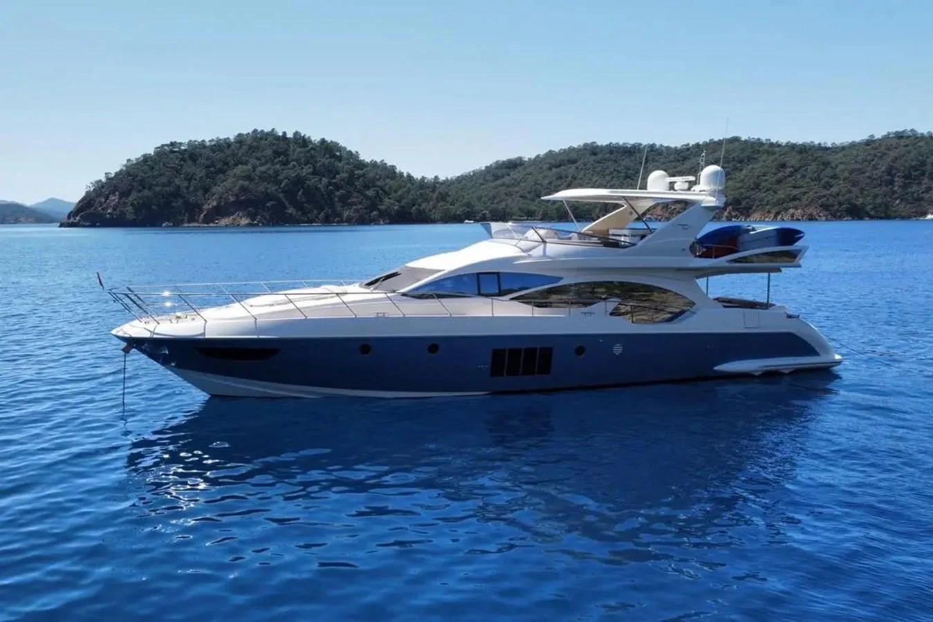 A sleek and modern yacht glides gracefully on calm blue waters with a scenic island backdrop. aboard NE SEL Yacht for Sale