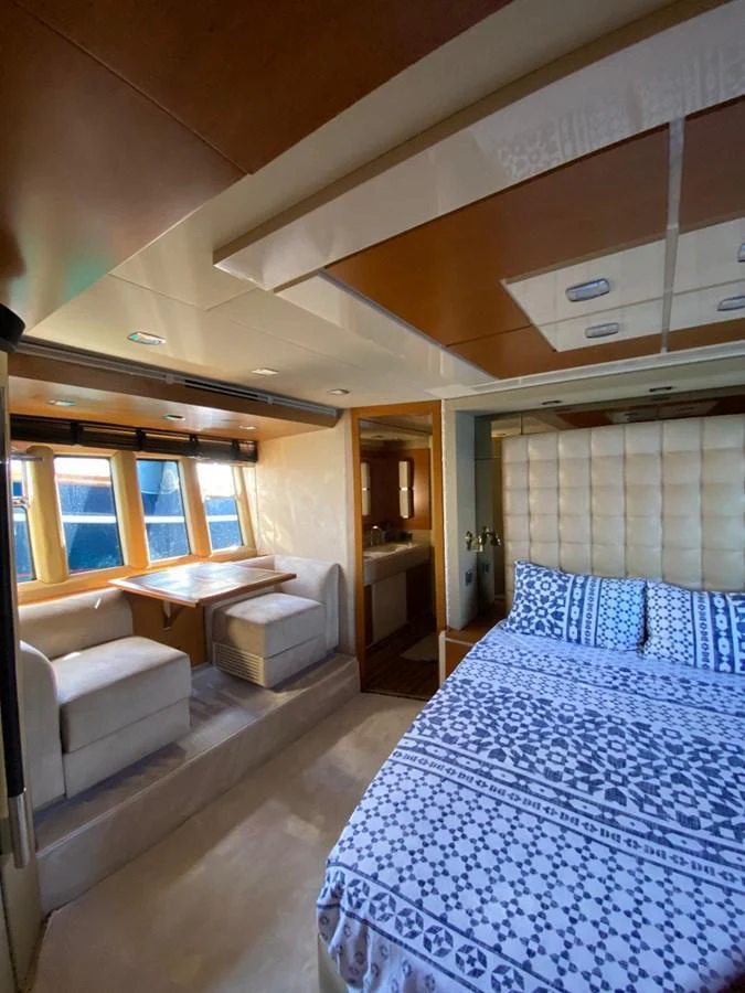 The stateroom features a cozy bed with patterned bedding and a seating area by the window. aboard NE SEL Yacht for Sale