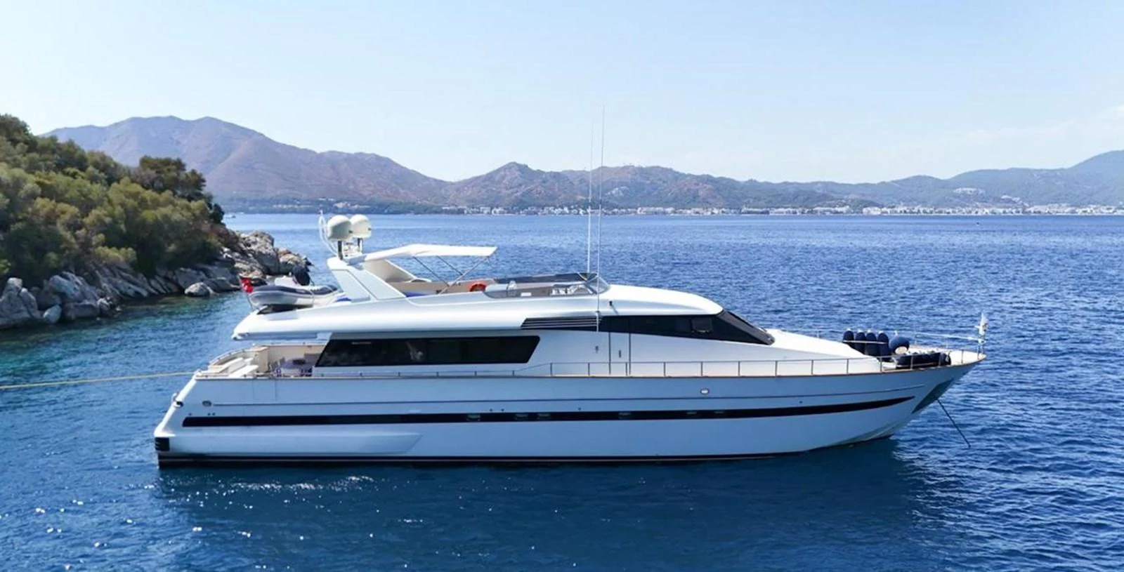 A sleek and modern yacht cruising in serene blue waters with a mountainous backdrop. aboard TWINS PC Yacht for Sale