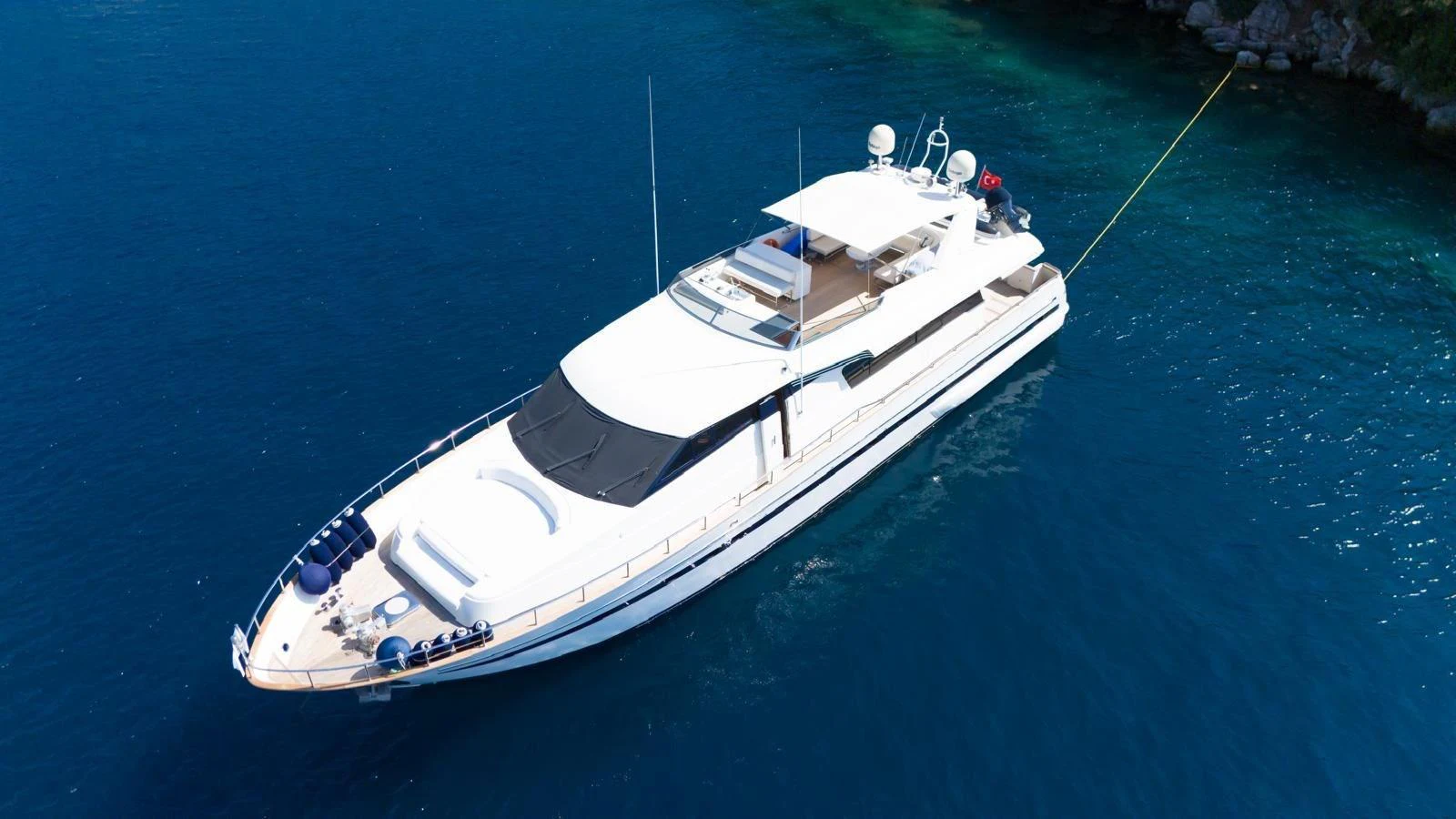 A sleek and modern yacht is anchored in clear blue waters, showcasing its elegant design and spacious deck areas. aboard TWINS PC Yacht for Sale
