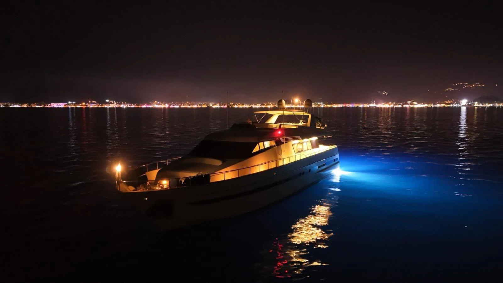 A luxurious yacht is illuminated against the night sky, reflecting lights on the calm water. aboard TWINS PC Yacht for Sale