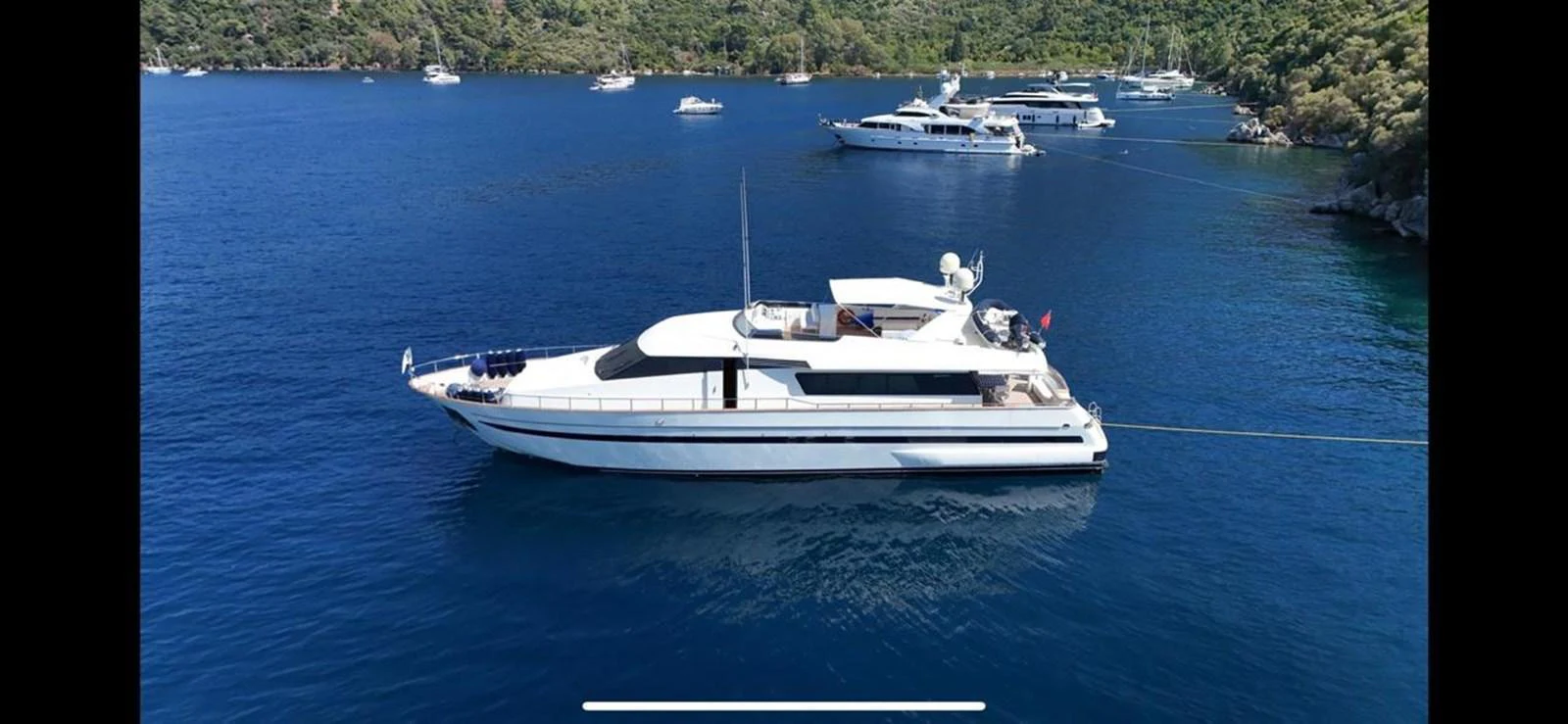 A sleek and modern yacht is anchored in a serene bay with lush greenery in the background. aboard TWINS PC Yacht for Sale