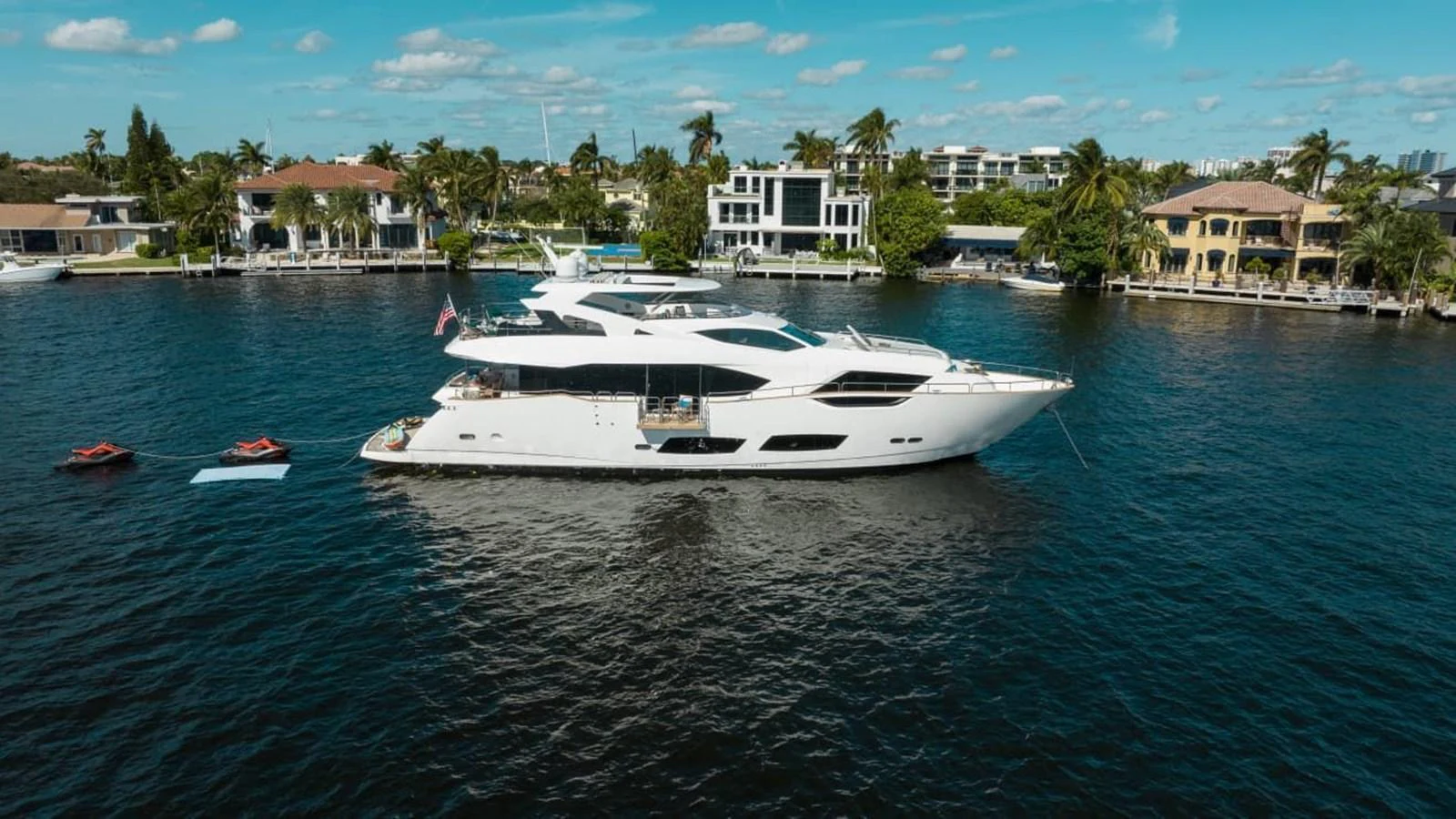 A sleek white yacht is anchored in a serene waterfront neighborhood, showcasing its elegant design and spacious decks. aboard 95 FT 2018 SUNSEEKER 95 YACHT, MIRRACLE Yacht for Sale