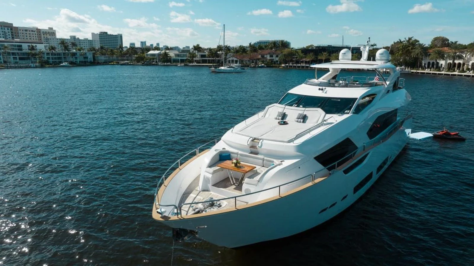 A luxurious yacht is anchored in a serene harbor with a beautiful cityscape in the background. aboard 95 FT 2018 SUNSEEKER 95 YACHT, MIRRACLE Yacht for Sale
