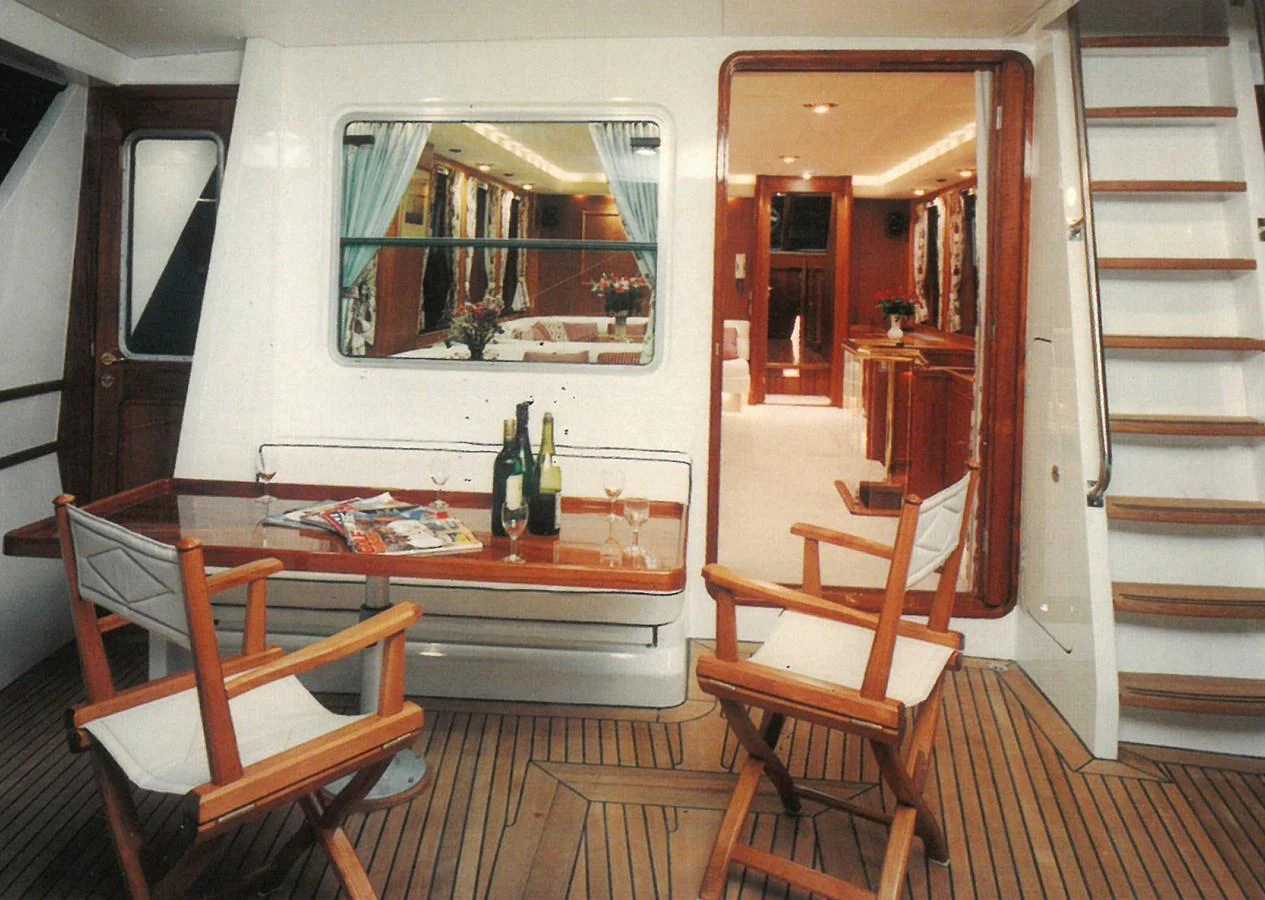 The aft deck features a cozy seating area with a table set for drinks, leading into a warmly lit interior. aboard REX AQUILA Yacht for Sale