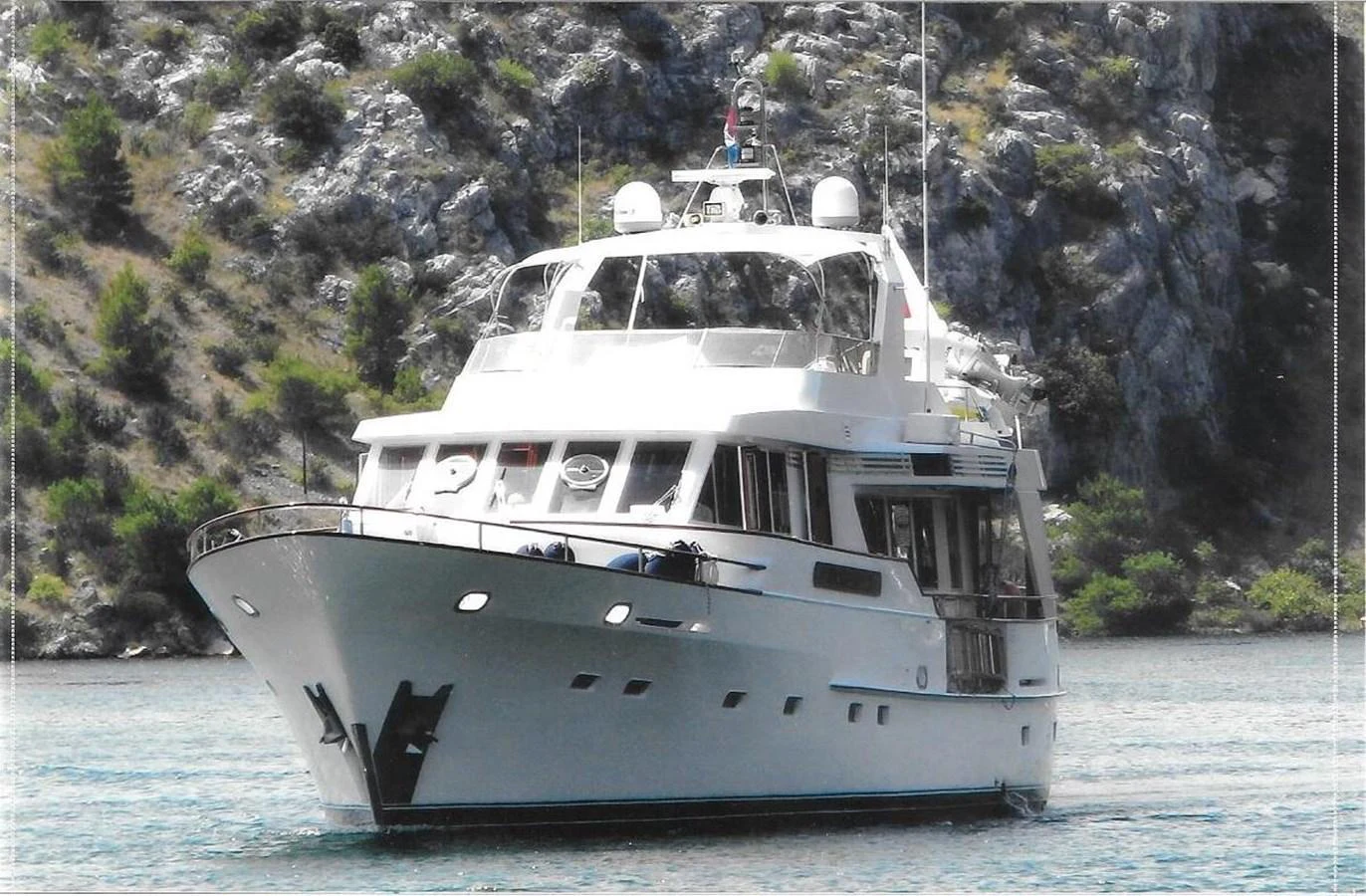 A classic motor yacht cruising in a serene, rocky coastal area. aboard REX AQUILA Yacht for Sale