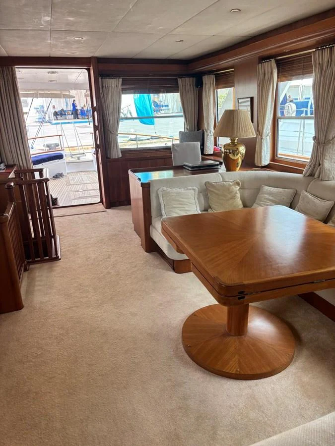The yacht's salon features a cozy seating area with a wooden table and large windows offering a view of the exterior deck. aboard REX AQUILA Yacht for Sale
