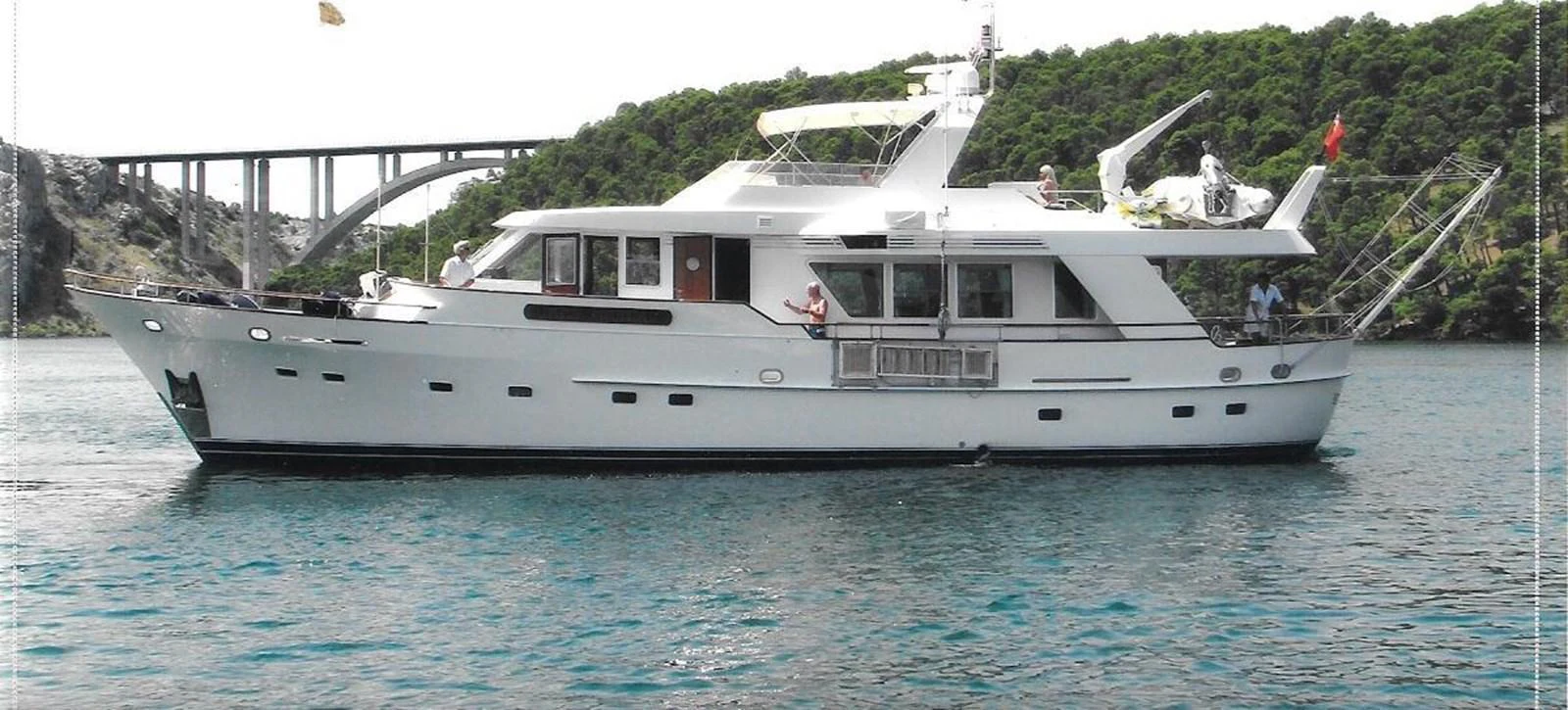 A classic motor yacht cruising on calm waters with lush greenery in the background. aboard REX AQUILA Yacht for Sale