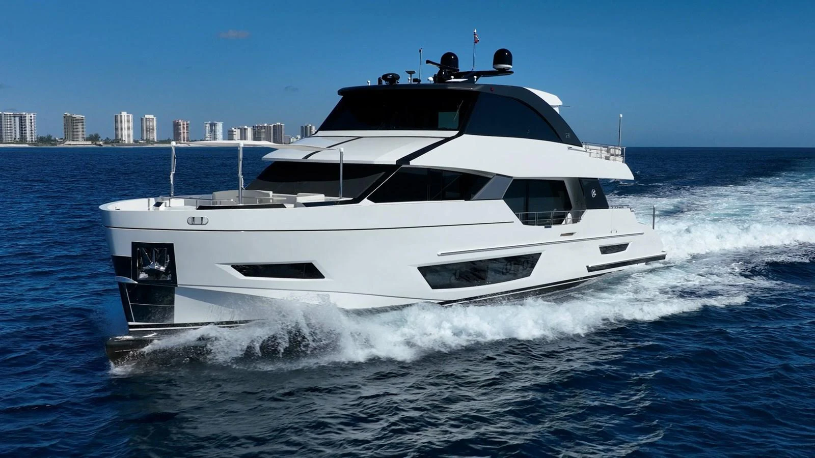 A sleek, modern yacht cruises through the open water with a cityscape in the background. aboard AQUASITION Yacht for Sale