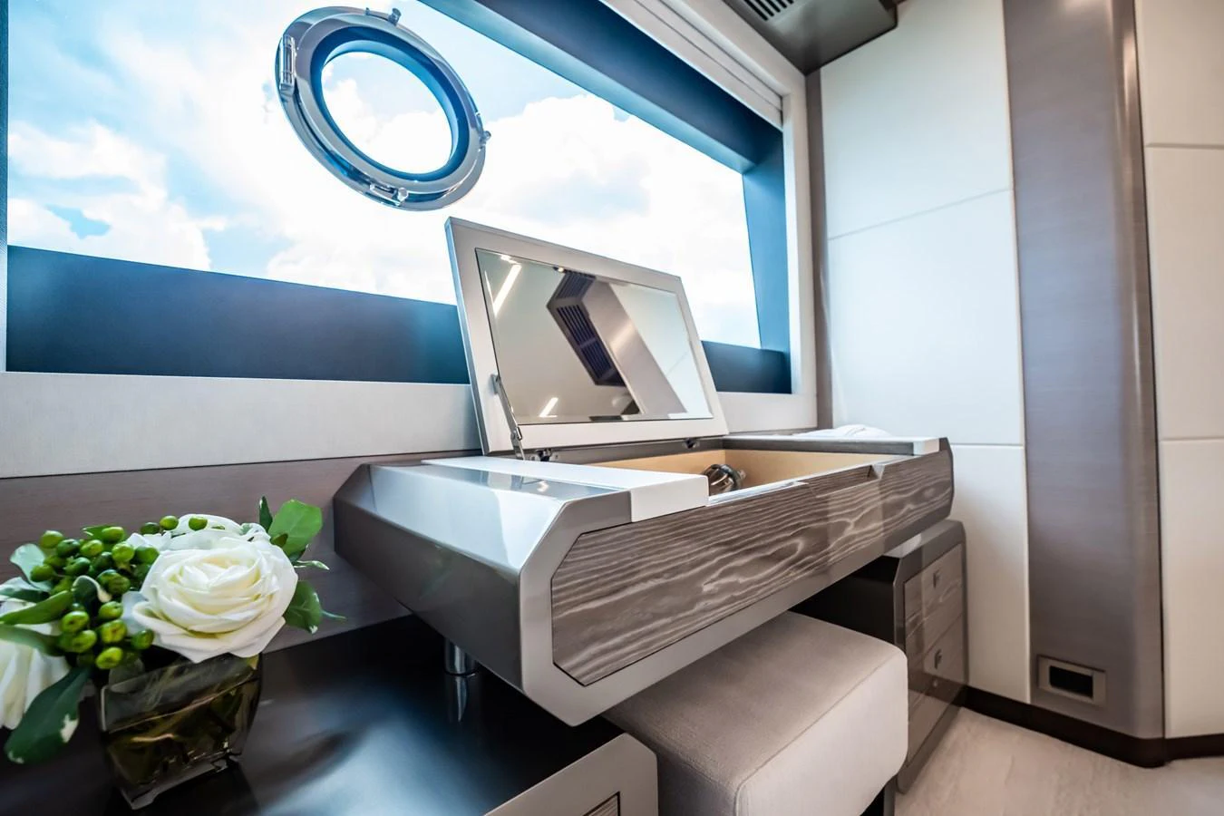 A luxurious vanity area with a mirror and a porthole window offering a view of the sky. aboard AQUASITION Yacht for Sale