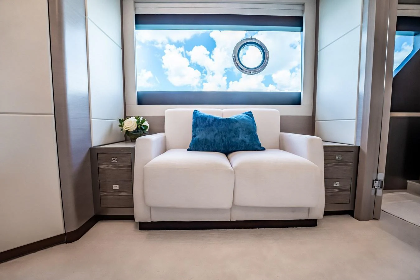A cozy seating area with a white sofa and blue pillow, complemented by a porthole window offering a view of the sky. aboard AQUASITION Yacht for Sale
