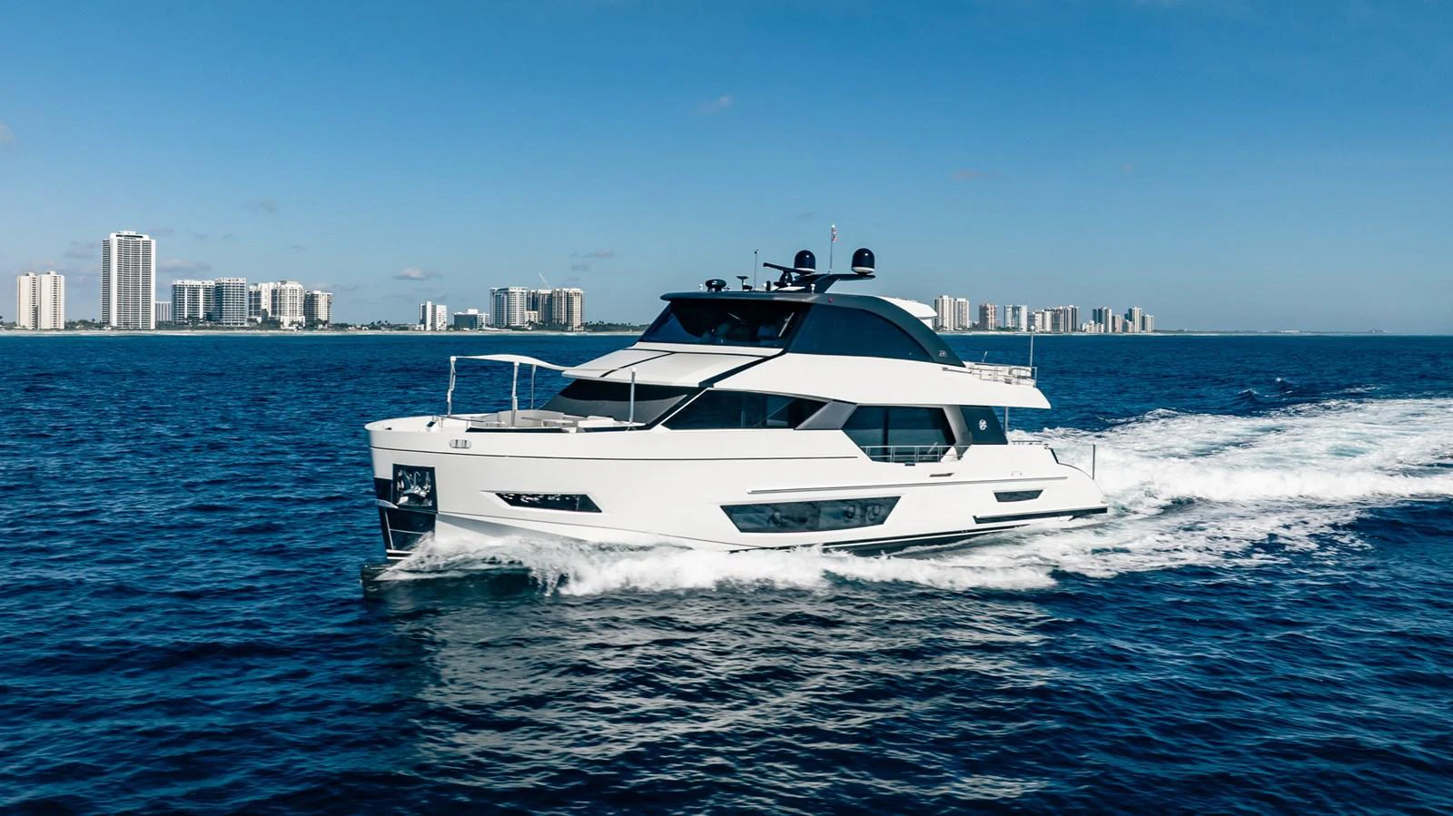 A sleek, modern yacht cruises through the open water with a cityscape in the background. aboard AQUASITION Yacht for Sale