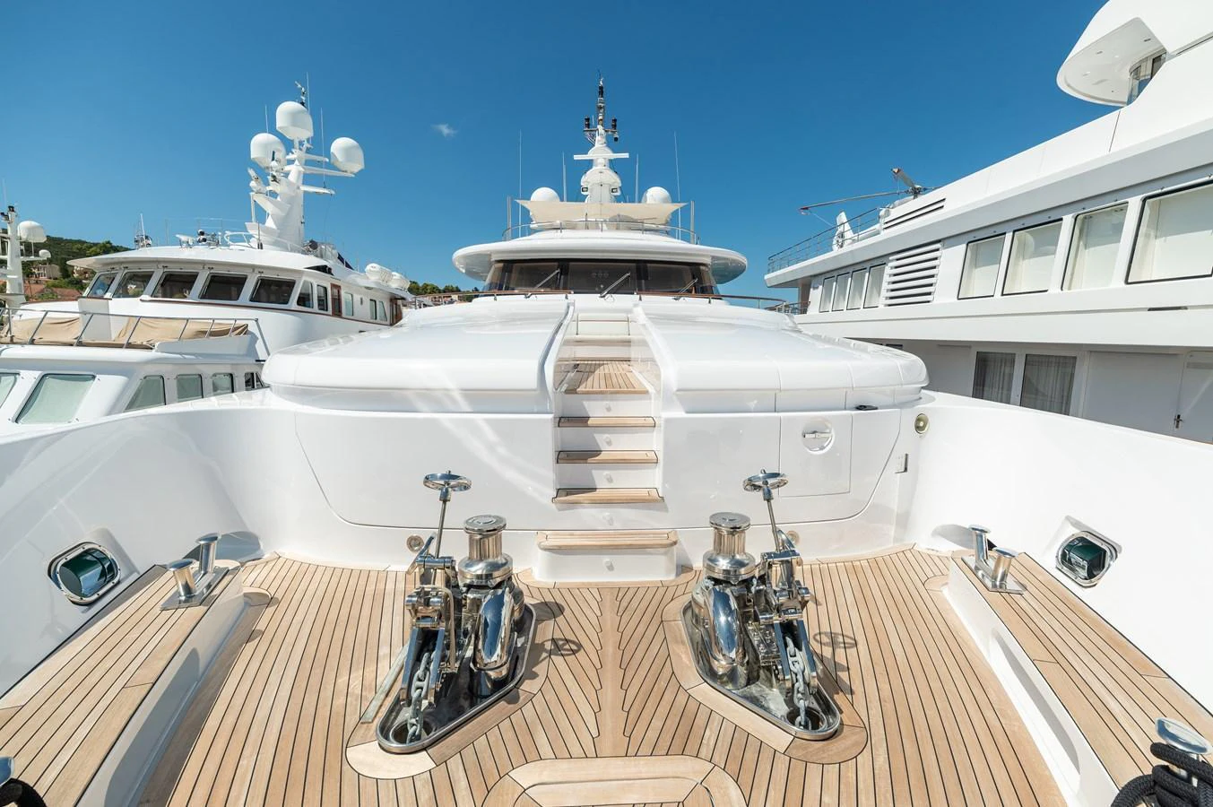 The yacht's foredeck showcases a pristine teak deck with polished stainless steel fittings under a clear blue sky. aboard EMOTION 2 Yacht for Sale