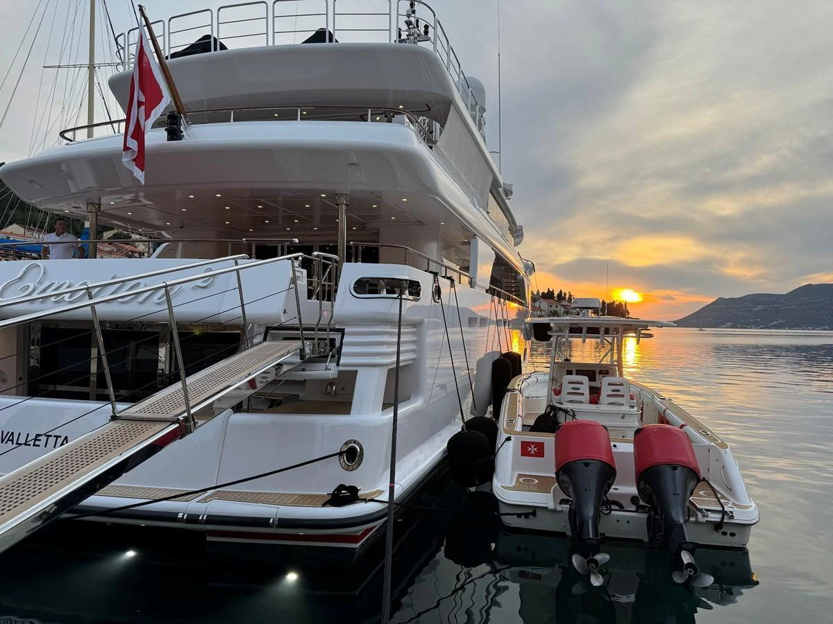 The yacht's aft deck is beautifully illuminated at sunset, with a tender moored alongside. aboard EMOTION 2 Yacht for Sale