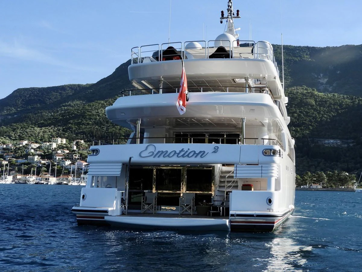 A luxurious yacht is anchored in a serene bay with lush green hills in the background. aboard EMOTION 2 Yacht for Sale