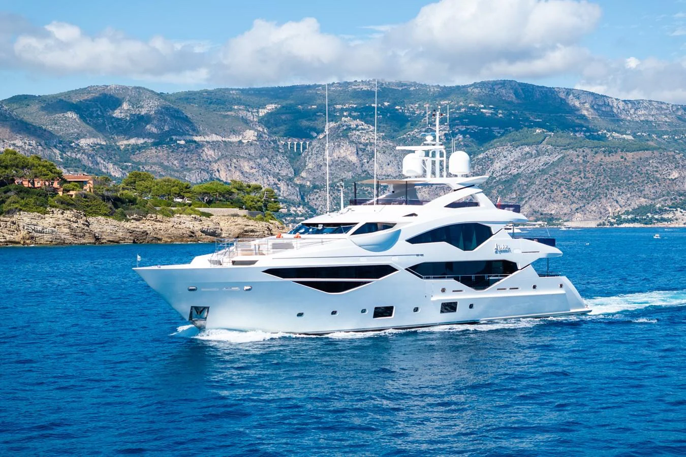 A luxurious yacht cruises through pristine blue waters against a backdrop of scenic mountains. aboard ALADDIN Yacht for Sale